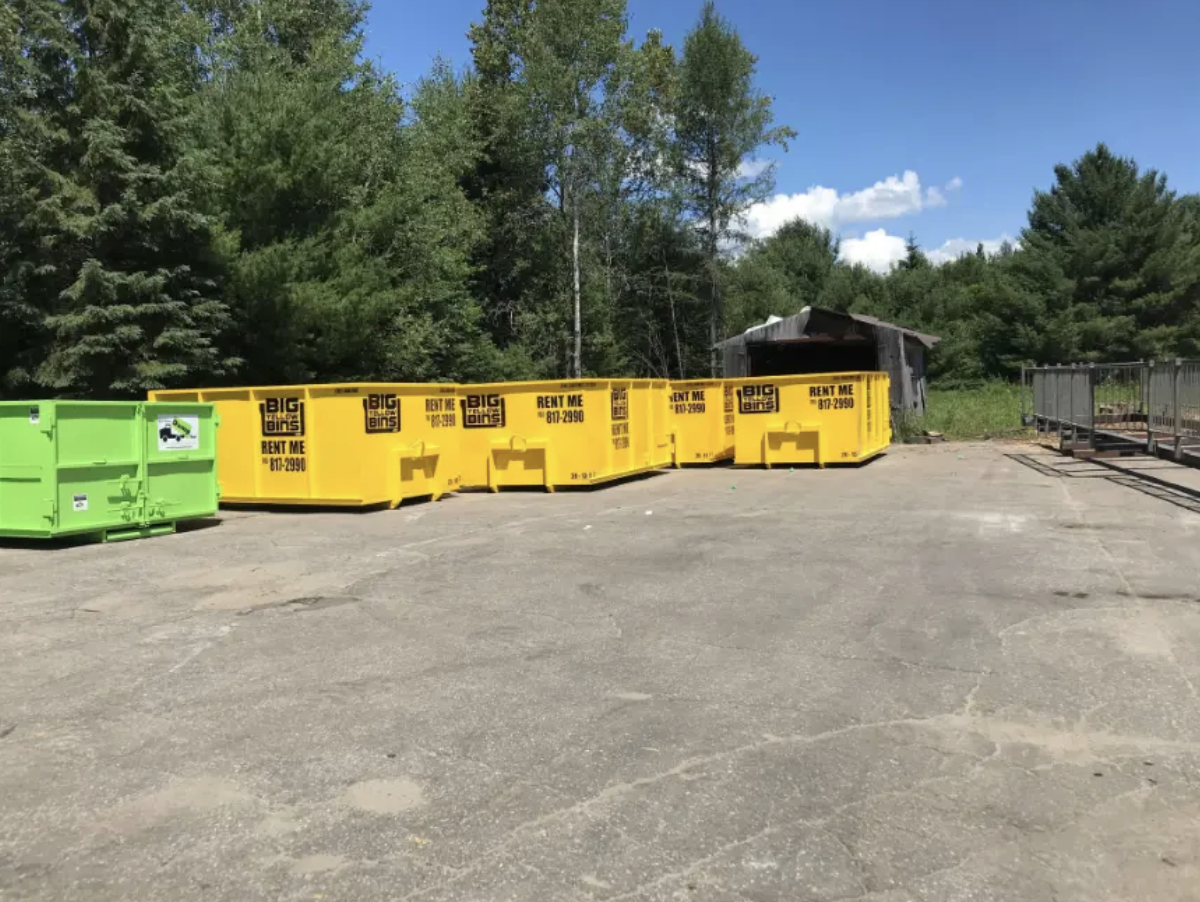 A row of yellow Big Yellow Bins roll-off bins lined up on a paved yard ready for delivery across Simcoe County