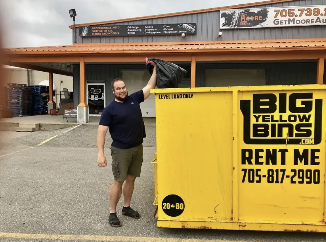 A customer tossing a garbage bag into a yellow Big Yellow Bins rental bin outside a commercial building in Simcoe County